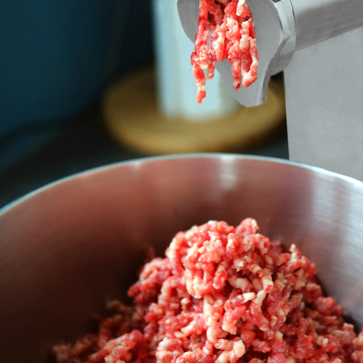Carne moída fresca sendo processada em um moedor de carne prateado, com textura suculenta e cor vermelha vibrante em uma tigela de metal