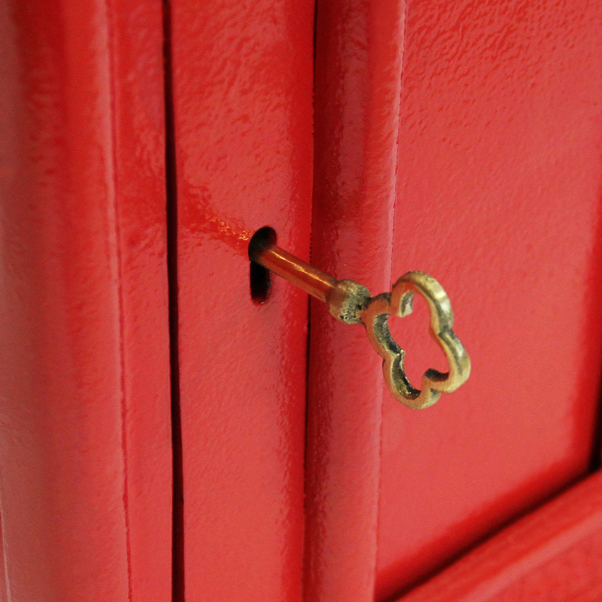 Caixa de correio Royal Mail vermelha com suporte, destacando a textura brilhante e a chave dourada em forma de nuvem