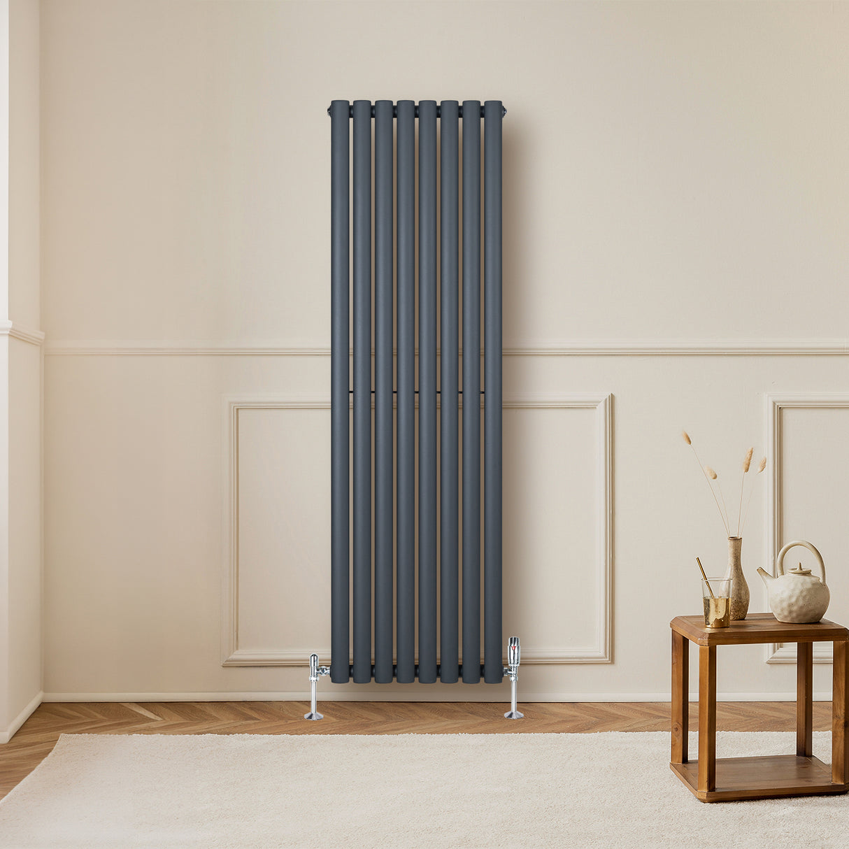 Radiador de coluna simples oval cinza antracite, com válvulas, instalado em parede clara, ao lado de mesa de madeira decorativa