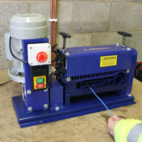 Máquina azul de desencapar fios com motor cinza, botões coloridos e cabo azul sendo inserido, ideal para processamento de cabos