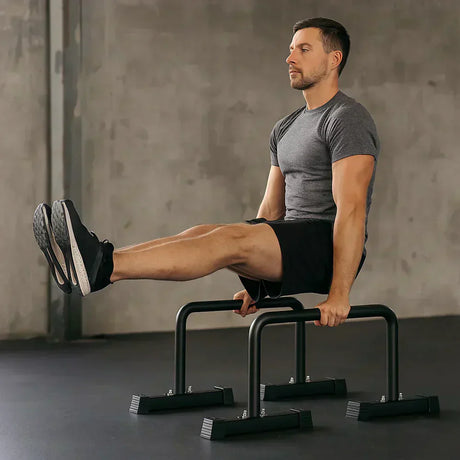 Homem realizando exercício de calistenia em barras paralelas, vestindo camiseta cinza e shorts pretos, em ambiente minimalista e moderno