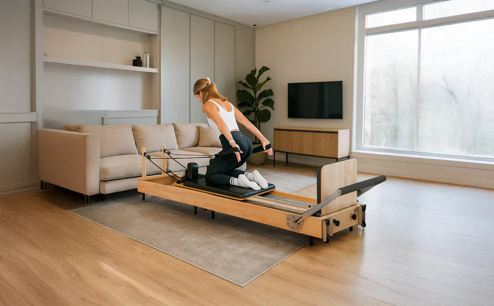 Mulher praticando Pilates em um reformer de madeira clara, em sala moderna com sofá e janela grande iluminando o ambiente