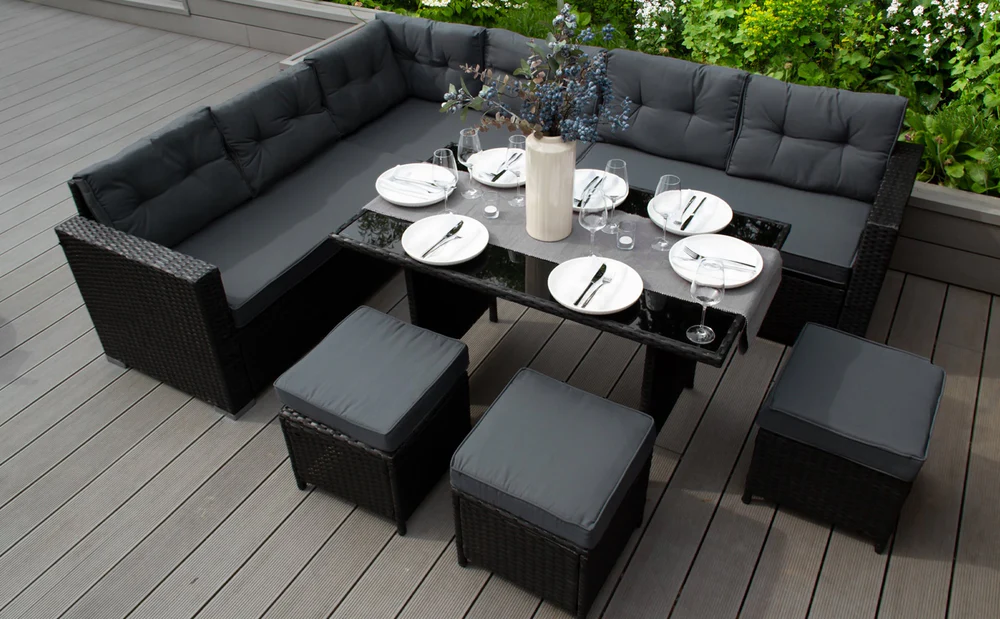 Conjunto de móveis de rattan preto com almofadas cinzas, mesa de vidro e decoração de flores em um ambiente ao ar livre