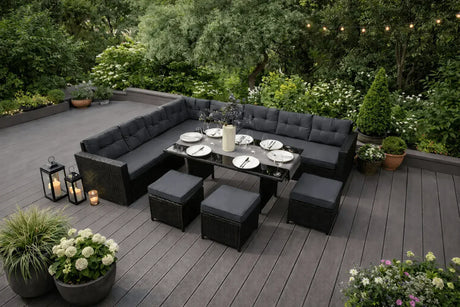 Conjunto de móveis de jardim em tons de preto, com mesa de vidro, almofadas cinzas e plantas ao redor, ideal para refeições ao ar livre