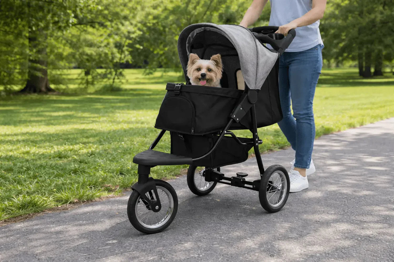 Carrinho de bebê para pets com design moderno, estrutura preta e tecido cinza, transportando um cachorro feliz em um parque verdejante