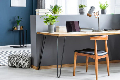 Mesa de madeira clara com pernas de hairpin, cadeira de madeira escura, laptop e plantas em vasos, ambiente moderno e minimalista