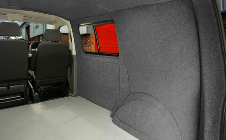 Interior de campervan com revestimento cinza escuro, bancos pretos e piso claro, destacando conforto e estilo minimalista