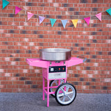 Máquina de algodão doce rosa com detalhes prateados, posicionada em frente a uma parede de tijolos, decorada com bandeirinhas coloridas