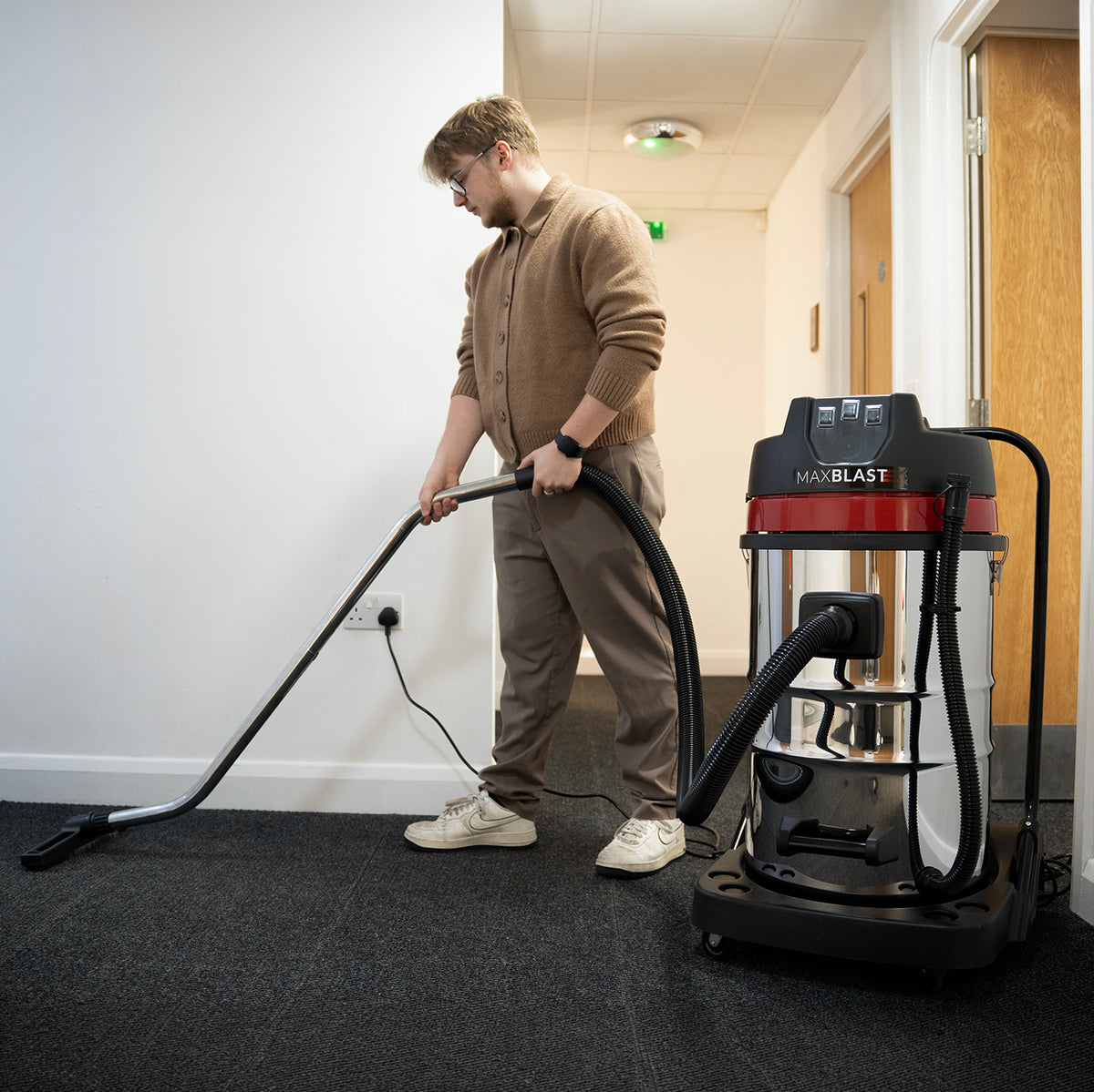 Aspirador comercial MAXBLAST de 80 litros, com design robusto, corpo prateado e detalhes em vermelho, sendo utilizado em ambiente interno