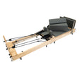 Reformer de Pilates dobrável em madeira de carvalho, com almofadas cinzas e cordas ajustáveis, ideal para exercícios em casa