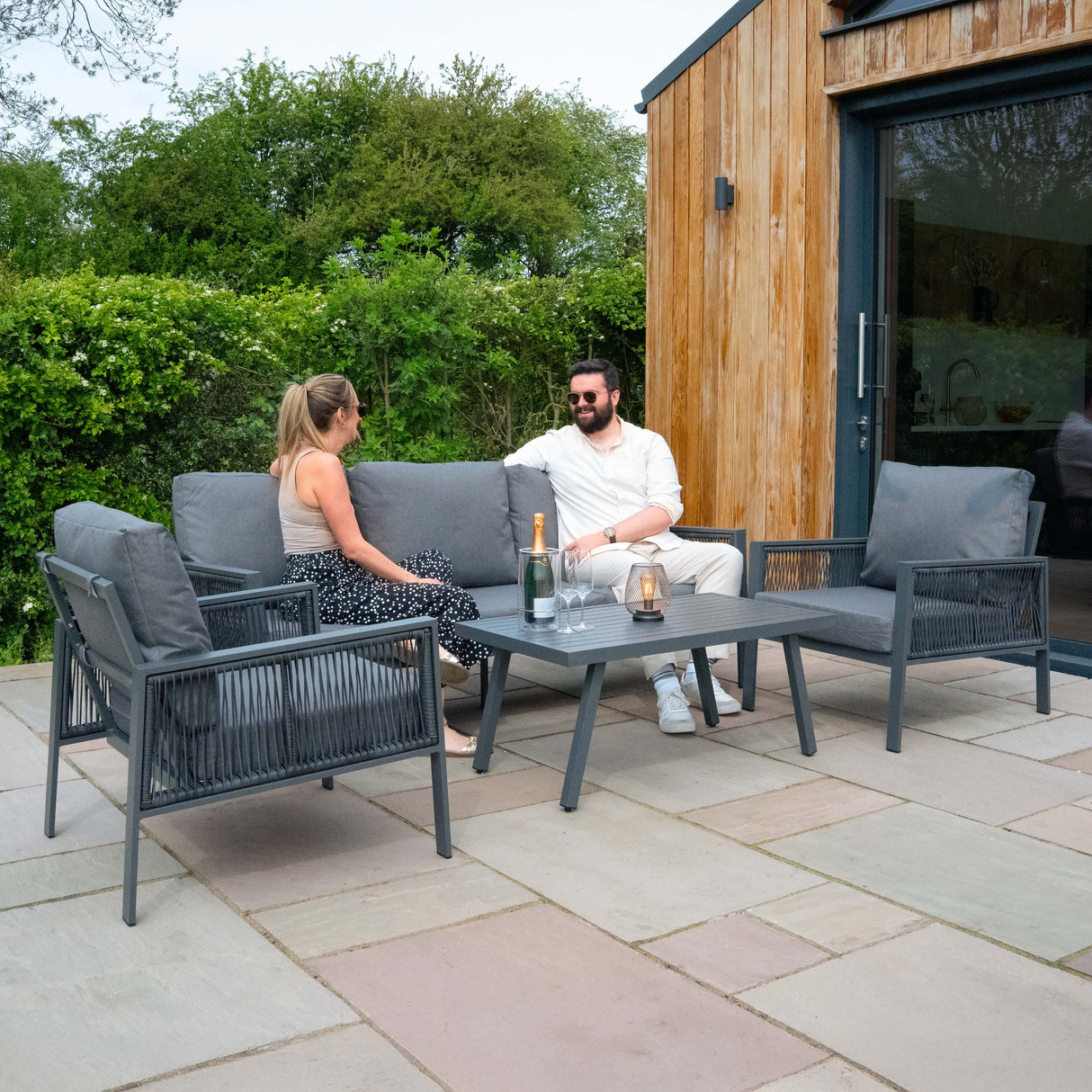Conjunto de sofá antracite de 4 peças com almofadas cinzas, mesa de centro e guarda-sol preto em ambiente externo relaxante