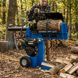 Rachador de lenha azul com motor potente, cortando troncos em um ambiente natural com folhas secas e árvores ao fundo