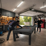 Mesa de jogos 7 em 1 cinza, com superfície de feltro, dardos e luz LED, em ambiente de garagem com ferramentas e bicicletas ao fundo