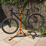 Suporte de oficina para bicicletas em preto e laranja, com estrutura estável e ajustável, ideal para manutenção e reparos