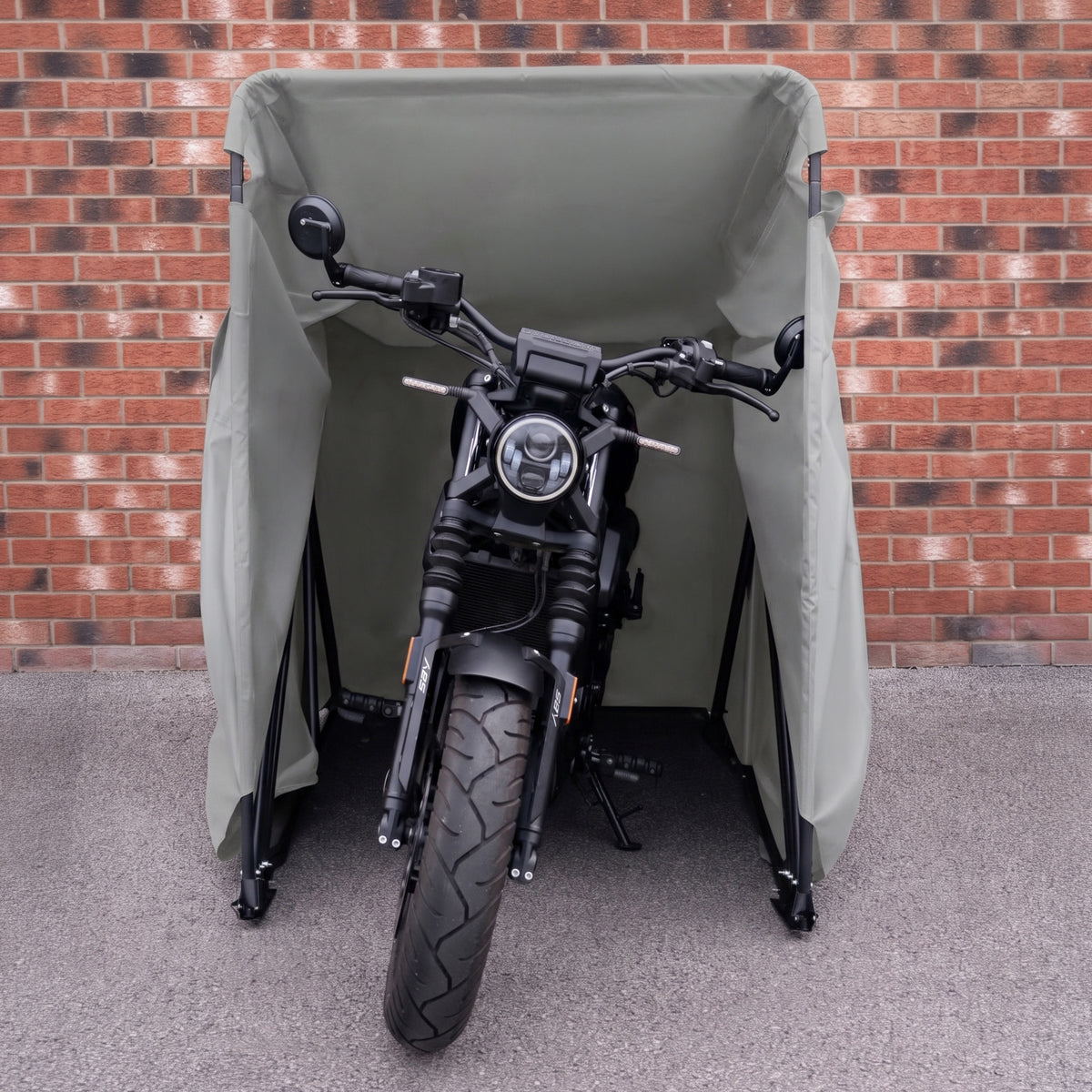 Moto preta estacionada sob uma capa verde, com detalhes em metal e pneus largos, em frente a uma parede de tijolos vermelhos