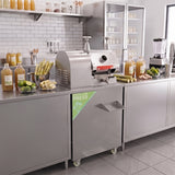 Máquina de suco de cana de aço inoxidável com design moderno, localizada em uma cozinha organizada, cercada por garrafas e cana-de-açúcar