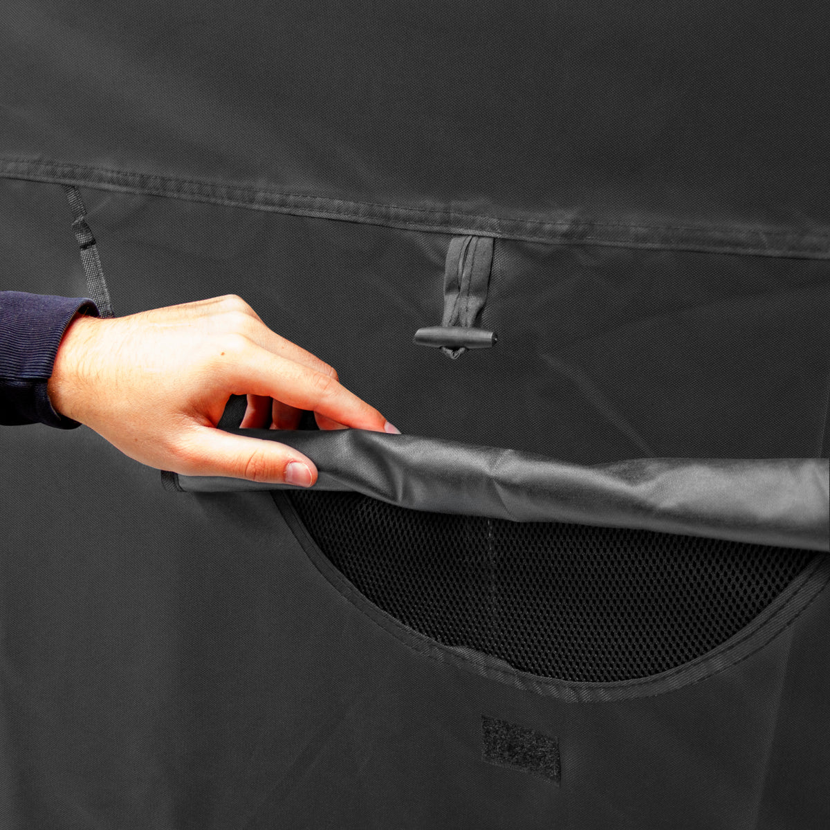 Bolsa de armazenamento em tecido preto, com bolso de malha e fechamento em velcro, sendo segurada por uma mão masculina