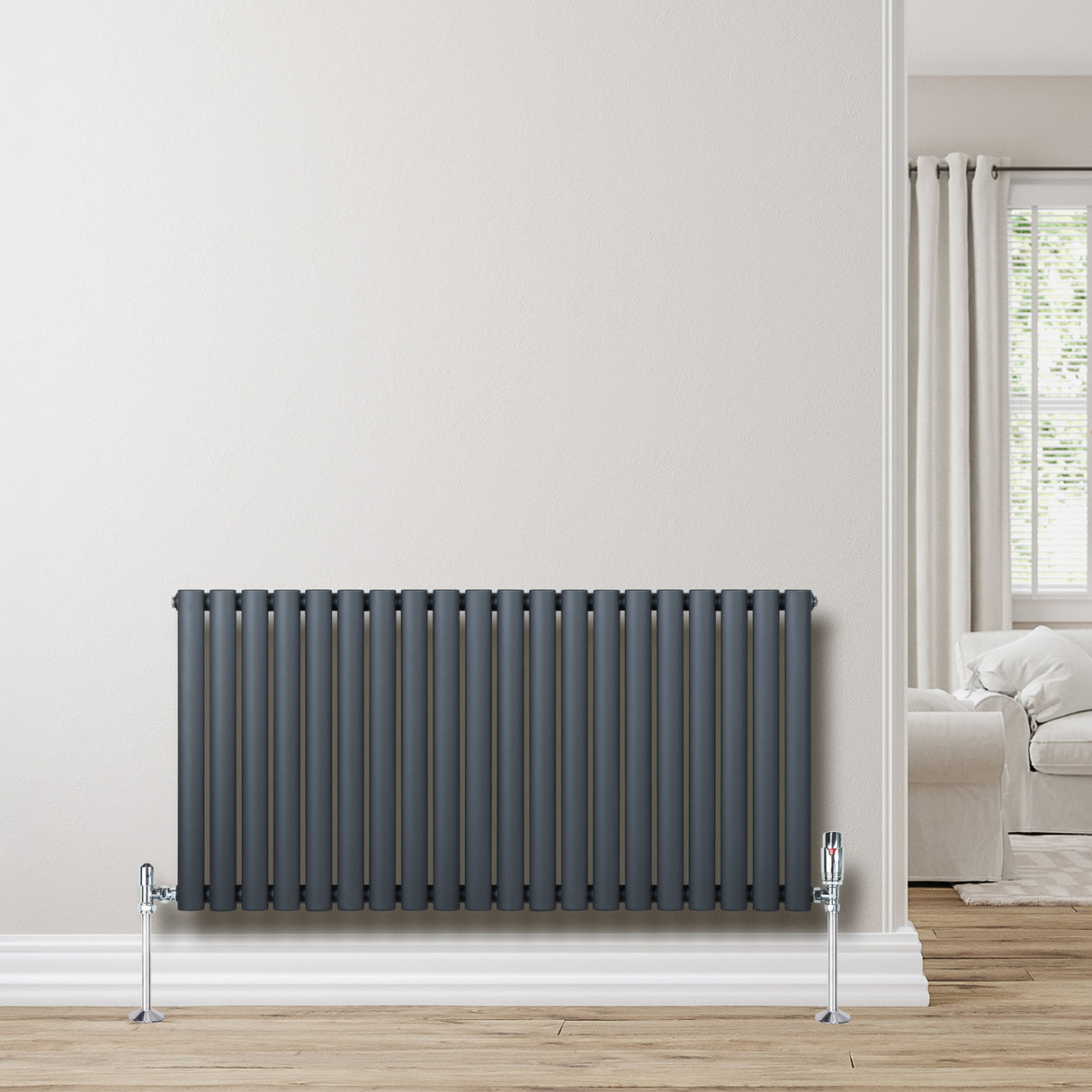 Radiador de coluna oval cinza antracite, com design moderno e válvulas cromadas, instalado em parede clara, ambiente aconchegante