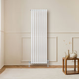 Radiador de coluna oval branco, com válvulas, instalado em parede clara, destacando seu design elegante e moderno em ambiente aconchegante