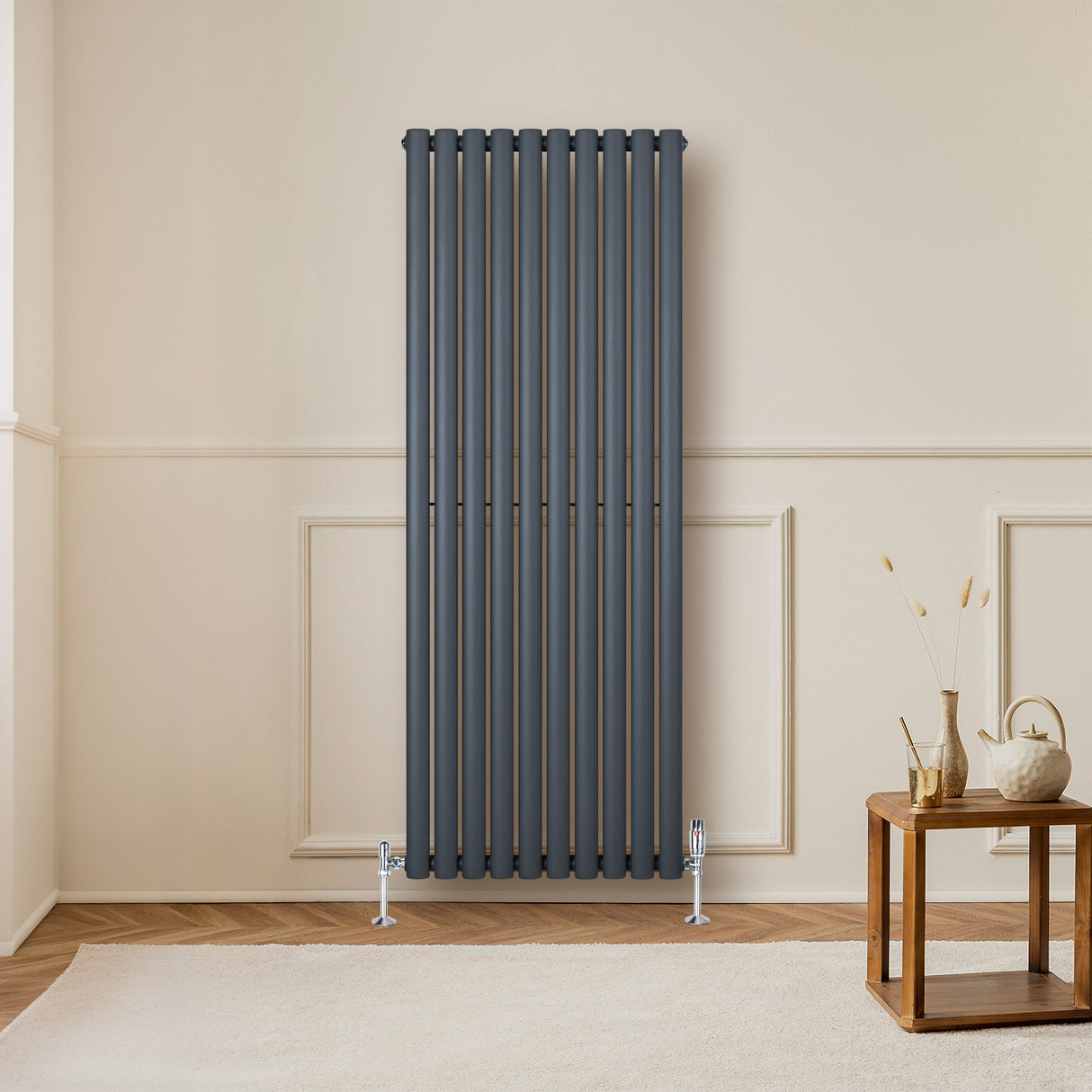 Radiador de coluna oval cinza antracite, 1600 mm x 600 mm, com válvulas, instalado em parede clara, ao lado de mesa de madeira