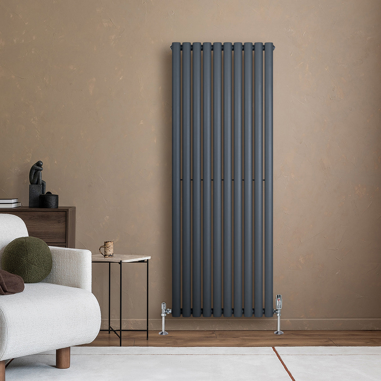 Radiador de coluna oval cinza antracite, com design vertical e válvulas, instalado em parede de tom neutro, ao lado de sofá moderno