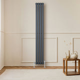 Radiador de coluna simples oval cinza antracite, com design elegante e acabamento liso, instalado em parede clara, ao lado de mesa de madeira