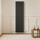 Radiador de coluna simples oval preto, com seis tubos verticais, instalado em parede clara, ao lado de mesa de madeira e decoração minimalista
