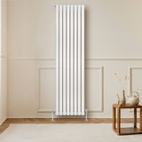 Radiador de coluna simples oval branco, com válvulas, medindo 1800 mm x 480 mm, instalado em parede clara, ao lado de mesa de madeira