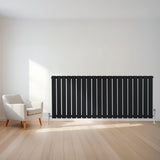 Radiador plano de coluna simples preto, com design elegante e moderno, instalado em parede clara, ao lado de poltrona confortável