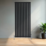 Radiador plano de coluna simples preto, com design vertical e válvulas, instalado em parede clara, ao lado de planta em vaso