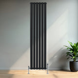 Radiador plano de coluna simples preto, com design vertical e válvulas, instalado em parede clara, ao lado de planta verde em vaso