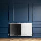 Radiador tradicional de 4 colunas, acabamento branco, com válvulas, instalado em parede azul, destacando seu design elegante e moderno
