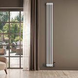 Radiador tradicional de 4 colunas, branco, instalado em parede cinza, com válvulas visíveis, ao lado de uma janela iluminada