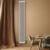 Radiador tradicional de 4 colunas em branco, instalado em parede bege, com válvulas visíveis e ambiente moderno com mesa e cadeiras
