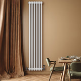 Radiador tradicional de 4 colunas, branco, instalado em parede, com válvulas visíveis, ao lado de mesa de jantar elegante e cortina marrom