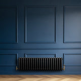 Radiador tradicional preto de 4 colunas, instalado em parede azul, com acabamento liso e detalhes em metal dourado nas conexões