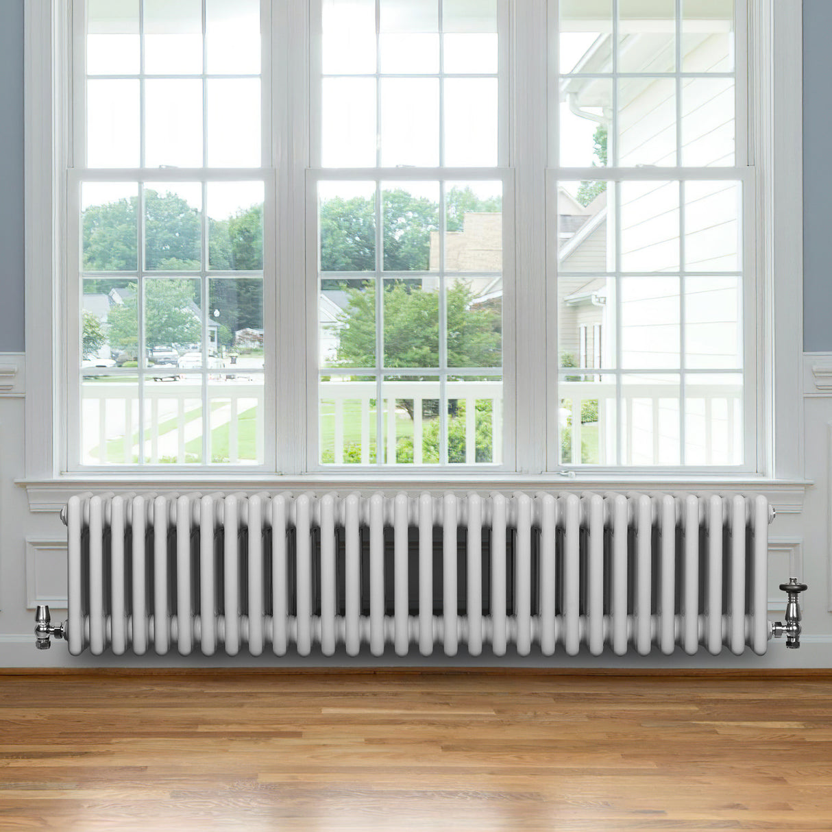 Radiador tradicional de 4 colunas, branco, com acabamento liso, instalado sob uma janela grande em ambiente iluminado e aconchegante