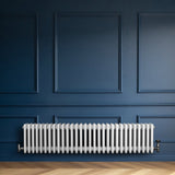Radiador tradicional de 4 colunas em branco, instalado em parede azul escura, com design elegante e acabamento liso, ideal para aquecimento