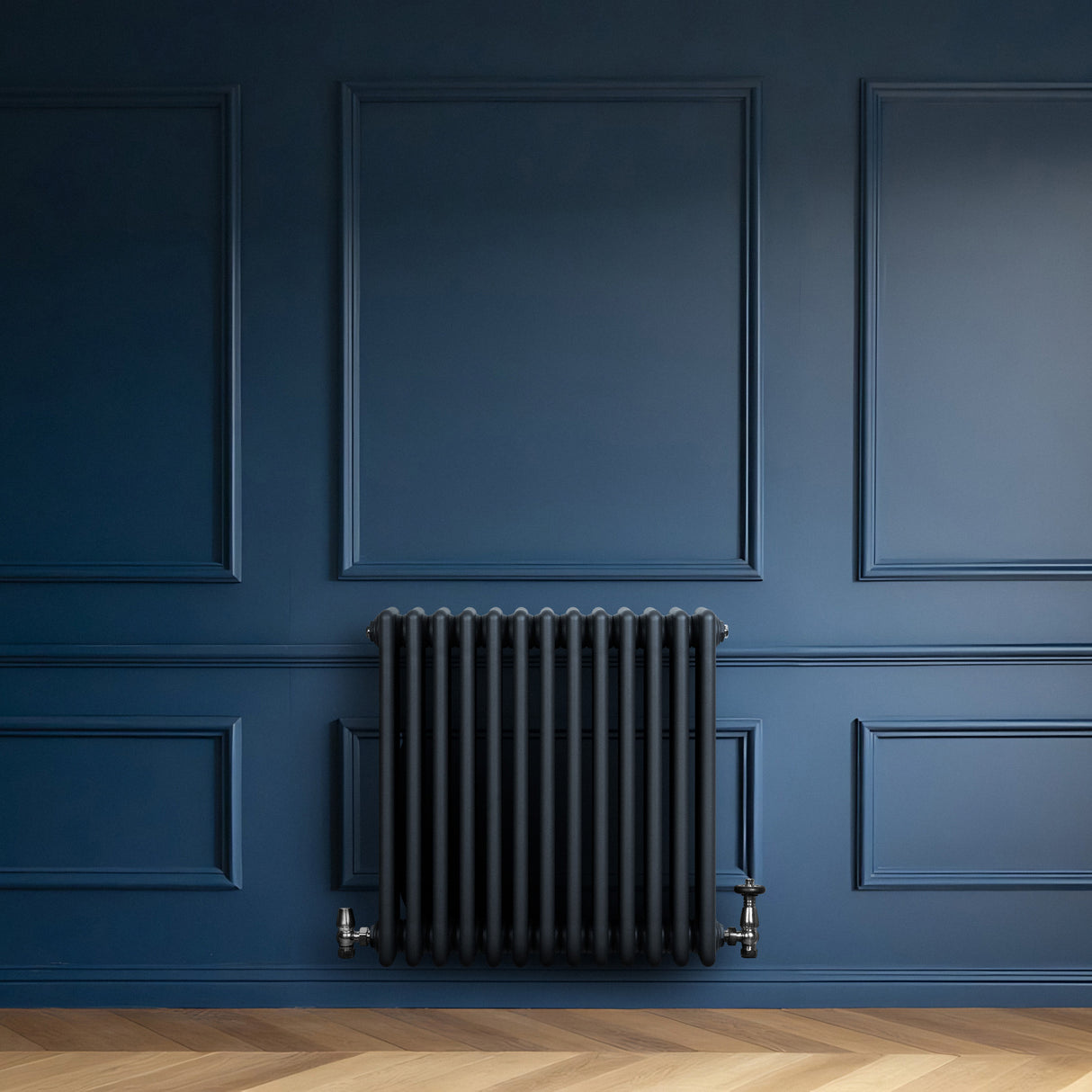 Radiador tradicional de 4 colunas em cinza antracite, instalado em parede azul escura, com textura lisa e design clássico