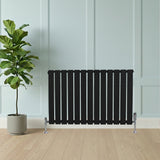 Radiador de coluna única preto, com design moderno e listras verticais, instalado em ambiente minimalista com planta ao lado