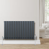 Radiador de coluna simples oval cinza antracite, com tubos verticais, instalado em parede clara, próximo a um sofá confortável
